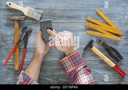 L'homme travaillant sur un projet de bricolage avec son téléphone, copeaux de bois et d'outils de menuiserie et de construction tout autour, en vue d'en haut Banque D'Images