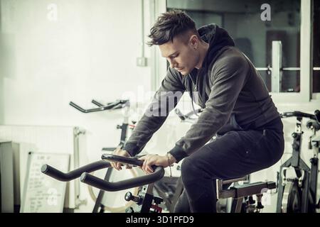 Jeune homme dans l'exercice de sport : spinning sur vélo stationnaire Banque D'Images