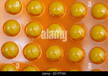 Les capsules jaune vif sont soigneusement placées sur un fond orange accrocheur. Banque D'Images