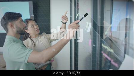 Collaborez avec des collègues dans le blazer et le polo sur panneau de verre avec tablette dans la salle de réunion Banque D'Images