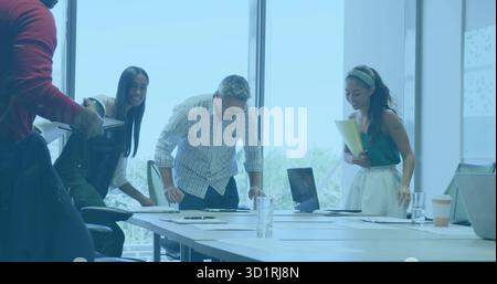 Employés penchés en tenue formelle examinant des documents sur une table de conférence, avec un ordinateur portable et une tablette Banque D'Images