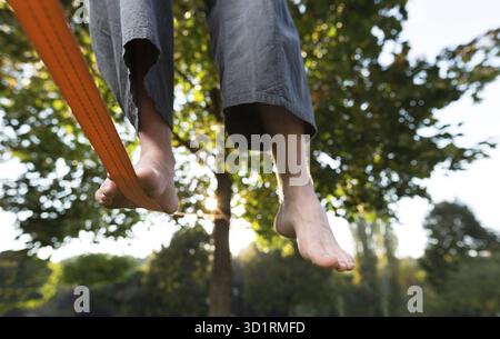 Gros plan des pieds d'homme équilibrant une corde serrée ou slackline dans un environnement de parc avec un pied au-dessus de la corde Banque D'Images