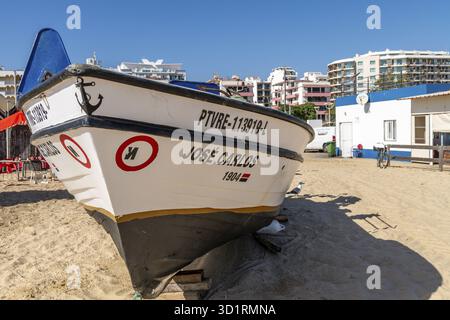 Monte Gordo, Faro - Portugal - 09-14-2024 : gros plan du bateau de pêche JOSE CARLOS 1904 reposant sur des supports en bois dans le sable avec une mouette, des bâtiments Banque D'Images