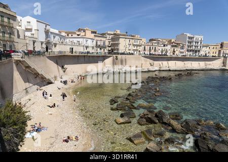 Syrakus, Sizilien - Italie - 04-09-2025 : petite plage à Syracuse avec eau turquoise claire, rivage rocheux, bains de soleil et bâtiments historiques Banque D'Images