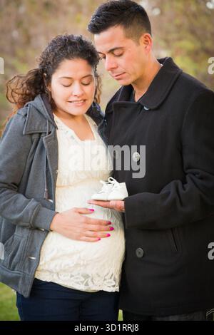 Couple hispanique enceinte tenant des chaussures de bébé Banque D'Images