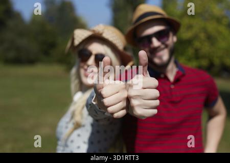 Vacances d'été, vacances, amour, geste et concept d'amitié - couple d'adolescents souriant dans des lunettes de soleil s'amusant et montrant les pouces vers le haut dans le parc Banque D'Images