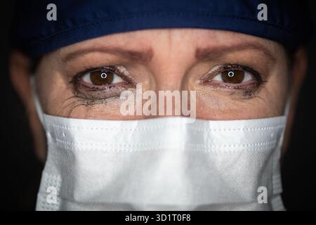 Médecin ou infirmière féminine stressée en larmes portant un masque facial médical sur fond sombre Banque D'Images