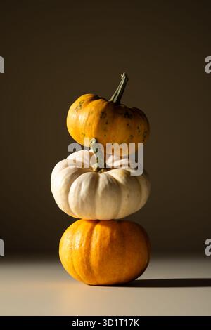Pile de petites citrouilles dans une lumière chaude sur un fond brun. Composition automnale minimaliste symbolisant l'équilibre, la simplicité et l'harmonie saisonnière. Banque D'Images