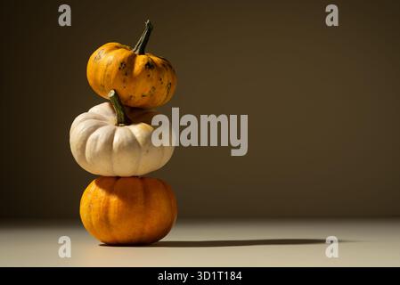 Pile de petites citrouilles dans une lumière chaude sur un fond brun. Composition automnale minimaliste symbolisant l'équilibre, la simplicité et l'harmonie saisonnière. Banque D'Images