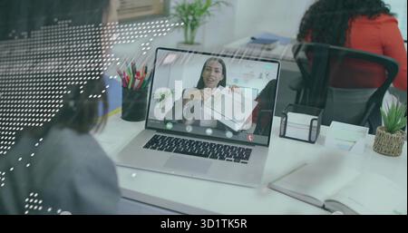 Femme d'affaires à distance portant un blazer gris montrant des graphiques dans le bureau, avec ordinateur portable, tasse à crayon, plante Banque D'Images