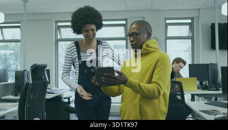 Discussion de contenu deux collègues examinent une tablette dans un bureau ouvert, avec des ordinateurs portables et des moniteurs Banque D'Images