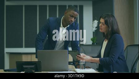 Deux collègues portant des blazers collaborant sur tablette dans la salle de réunion, avec ordinateur portable Banque D'Images