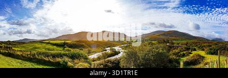 Vue panoramique sur la campagne irlandaise avec des champs verdoyants, une rivière qui coule et des montagnes lointaines sous un ciel spectaculaire Banque D'Images