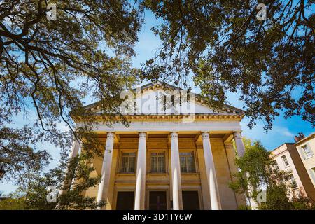 Église de style néo-grec, six hautes colonnes, « première église baptiste » gravée sur le fronton, encadrée par des branches de chêne feuillu, ciel bleu en arrière-plan Banque D'Images