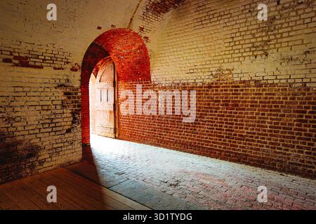 Intérieur du Fort Pulaski avec porte voûtée, murs en briques rouges et blanches altérées, double porte en bois partiellement ouverte, entrée de couloir voûtée Banque D'Images
