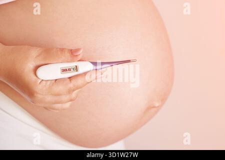 Femme enceinte tenant un thermomètre de fièvre. Traitement de la grippe. Corps humain. Femme malade à la maison Banque D'Images