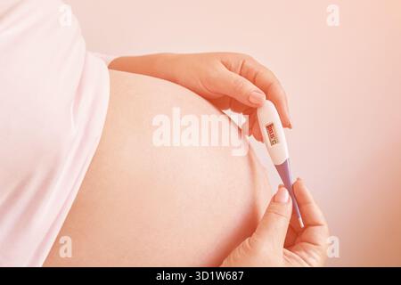 Femme enceinte tenant un thermomètre de fièvre. Traitement de la grippe. Corps humain. Femme malade à la maison Banque D'Images