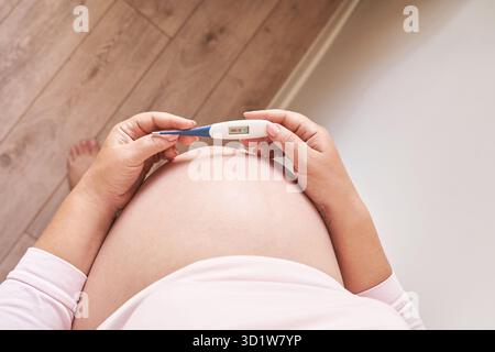 Femme enceinte tenant un thermomètre de fièvre. Traitement de la grippe. Corps humain. Femme malade à la maison Banque D'Images