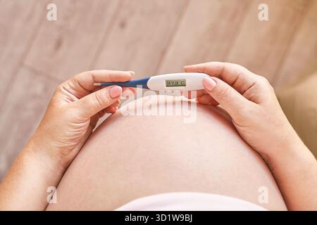 Femme enceinte tenant un thermomètre de fièvre. Traitement de la grippe. Corps humain. Femme malade à la maison Banque D'Images