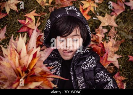 vue supérieure d'une fille grimacante couchée au milieu de feuilles d'automne rouges et jaunes Banque D'Images