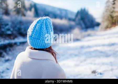 Vue arrière portrait d'une femme voyageuse admirant les montagnes enneigées et la vue sur la rivière portant un manteau de fourrure blanc chaud. Paysage forestier glacial hivernal. Espace Banque D'Images