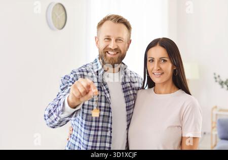 Heureux jeune couple tenant les clés de leur nouvelle maison, célébrant l'achat de biens immobiliers familiaux ensemble. Banque D'Images