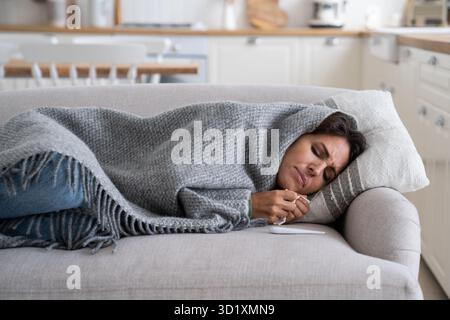 Le tissu de la femme malade contrarié couché sur le canapé à la maison a eu la grippe, ayant des symptômes de grippe, Banque D'Images