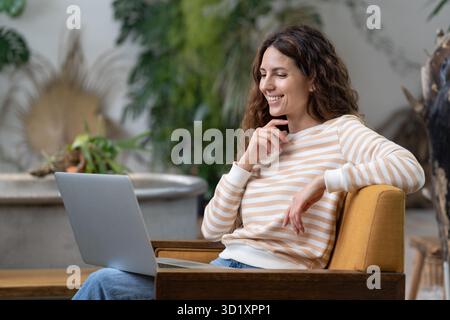 Une femme italienne s'est cououtrée et a passé un appel vidéo sur un ordinateur portable, assis dans un fauteuil dans un confortable jardin Banque D'Images