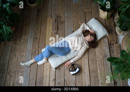 Femme millénaire détendue rêvant après avoir utilisé l'interface de réalité virtuelle, vue de dessus Banque D'Images