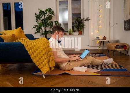 Homme sérieux travailleur indépendant travaillant sur ordinateur portable dans l'obscurité à la maison regardant l'écran. Banque D'Images