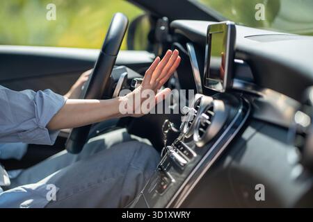 La main féminine vérifie le débit d'air froid du climatiseur à l'intérieur de la voiture, souffre de la chaleur dans le véhicule Banque D'Images