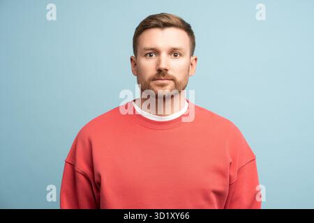 Triste homme inquiet avec l'expression sérieuse du visage se tient debout regardant la caméra sur fond bleu dans le studio Banque D'Images