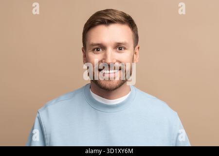Portrait, photo de studio d'homme barbu caucasien regardant la caméra souriant sur fond beige. Banque D'Images