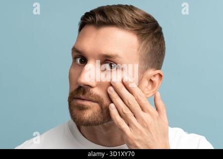Portrait d'un homme d'âge moyen barbu sérieux regardant les rides sous les yeux touchant la peau du visage. Banque D'Images
