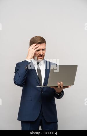L'homme a des problèmes dans les affaires, de mauvais résultats financiers en regardant l'ordinateur portable sur fond gris. Banque D'Images