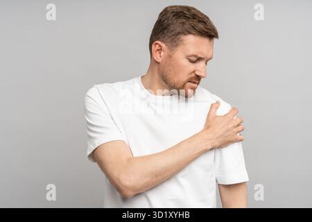 Homme d'âge moyen touchant la main épaule ressentant une douleur isolée sur fond gris après une blessure. Banque D'Images