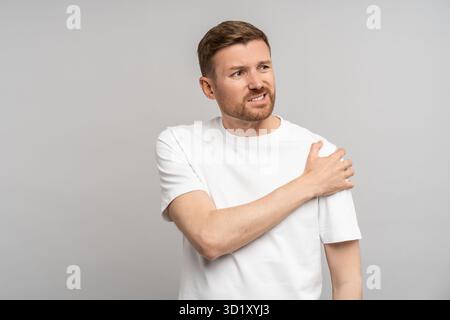 Homme d'âge moyen touchant la main épaule ressentant une douleur isolée sur fond gris après une blessure. Banque D'Images