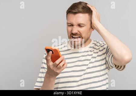 Tête d'embrayage d'homme choqué de nouvelles du téléphone, éprouvant l'échec avec le chagrin, isolé sur le mur de studio Banque D'Images