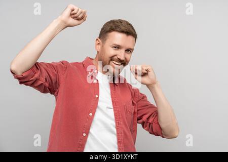 Homme souriant dansant dans la célébration heureuse, exprimant des émotions positives, isolé sur le mur du studio Banque D'Images