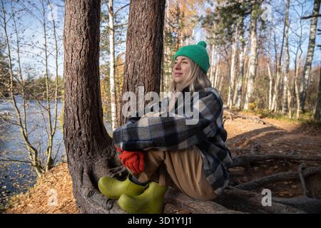 Femme d'âge moyen contemplant profiter de la nature dans la forêt assise sur les racines des arbres regarder dans la distance Banque D'Images