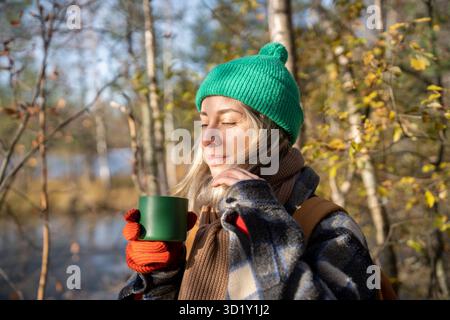 Recréer dans la forêt de pins femme d'âge moyen appréciant boire du thé chaud tout en se reposant après la randonnée Banque D'Images