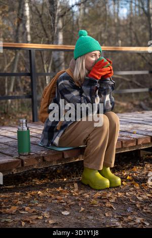 Femme d'âge moyen appréciant la boisson de thé chaud tout en se reposant après une randonnée sur un sentier en bois dans la forêt Banque D'Images