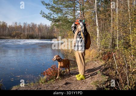 Heureuse voyageuse femelle, chien de chasse debout sur le rivage par l'eau de la rivière, marchant dans la forêt d'automne. Banque D'Images