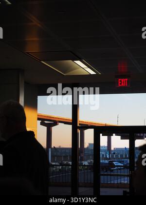 Intérieur de l'aéroport de Newark avec silhouettes et lumière du lever du soleil à travers les fenêtres donnant sur la chaussée surélevée Banque D'Images