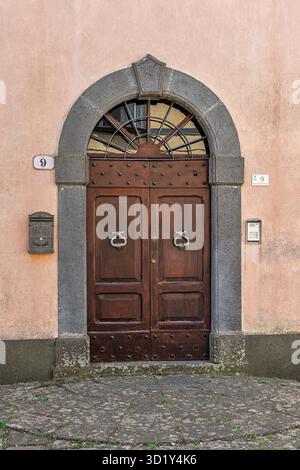 Italie - Bagnoregio - Centre historique - porte en bois voûtée dans le portail en pierre de tuf sombre situé dans la façade en stuc pâle au-dessus de la rue pavée Banque D'Images