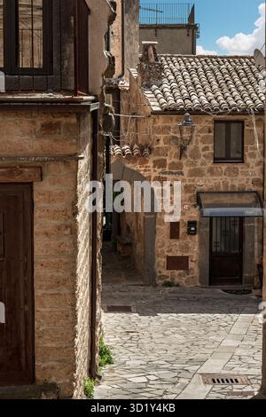 Italie - Bagnoregio - Centre historique - maisons rustiques en pierre avec arche sur rue pavée, volets et toits de tuiles encadrant une place tranquille Banque D'Images