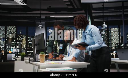 Groupe d'employés noirs faisant un travail d'équipe sur une tâche importante tard dans la nuit, collaborant à l'élaboration d'une nouvelle stratégie de développement après les heures de travail. Examiner les informations pour améliorer l'efficacité. Banque D'Images