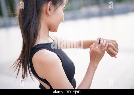 Femme asiatique sportive vérifiant le pouls dans la montre intelligente dans l'entraînement de vêtements de sport avec l'application de santé sur la montre intelligente après le bien-être d'exercice Banque D'Images