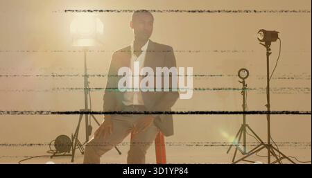 Homme noir assis sur le tabouret portant une tenue d'affaires dans le studio, avec des lumières, des câbles, des lignes de pépins Banque D'Images