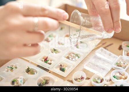 Mains versant de la résine dans des moules pour la fabrication artistique de bijoux à l'atelier d'artisanat Banque D'Images